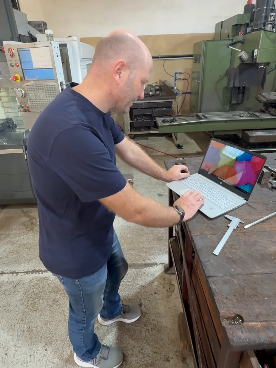 Max Pallotto at a laptop in a machine shop, with a Haas behind