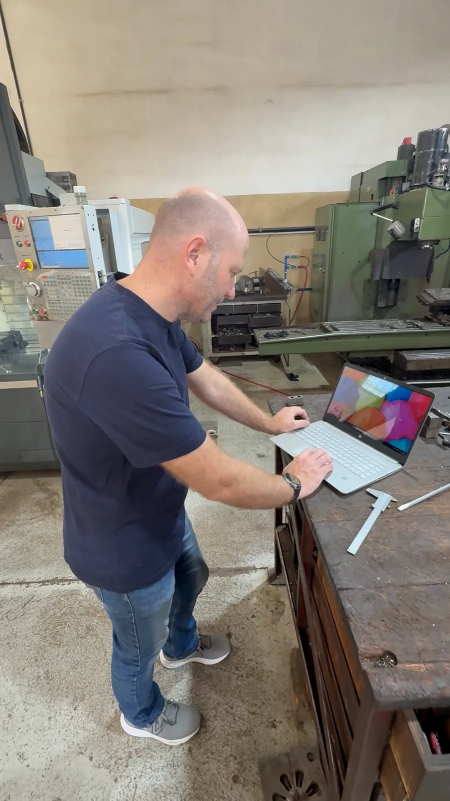 The programmer at a laptop on the shop floor, a Haas behind
