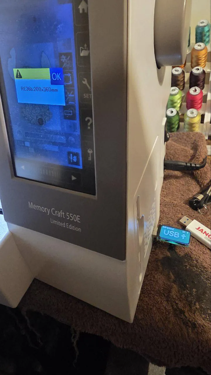 A Janome Memory Craft 550E Limited Edition with the WiFiDrive in USB mode in its USB port, its screen asking for the RE36b hoop for the design just opened